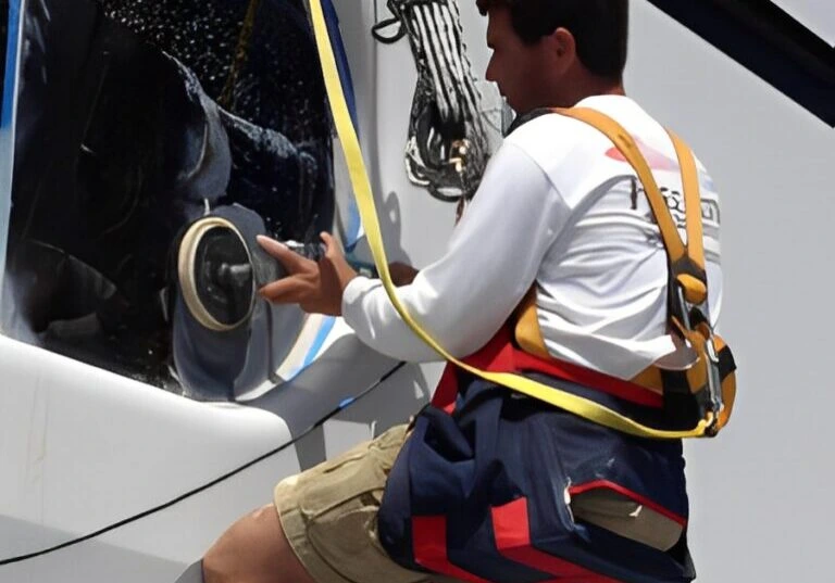 A man in a harness repairing the side of a yacht.