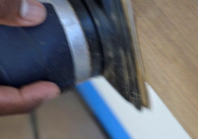 Hand using electric sander on wood surface.